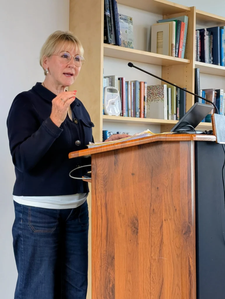A woman stands at a podium with bookshelves behind her.