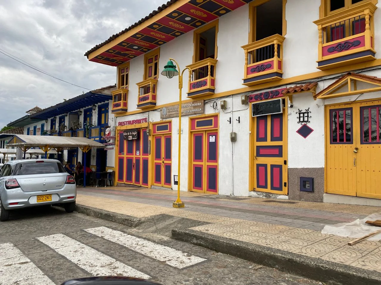 A colourful two story building by the road with a zebra crossing and a passing car