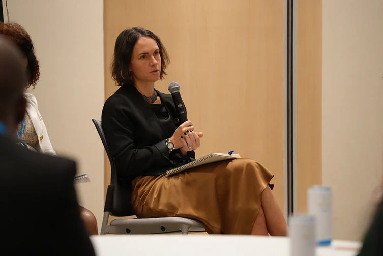 Marie Jürisoo sits on a panel, speaking into a microphone with a notebook on her lap.