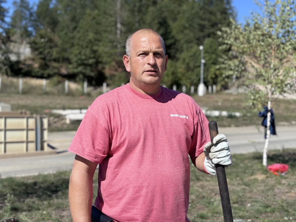 A man with red t-shirt standing and holding a shovel