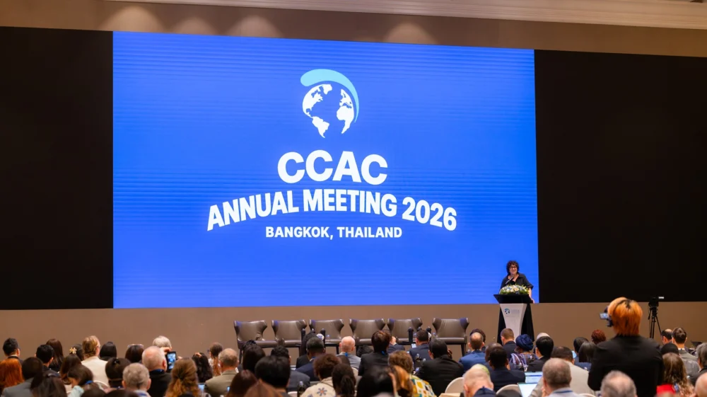 Martina Otto of the CCAC, standing on the stage in a black dress and blue backdrop decalring the conference open.