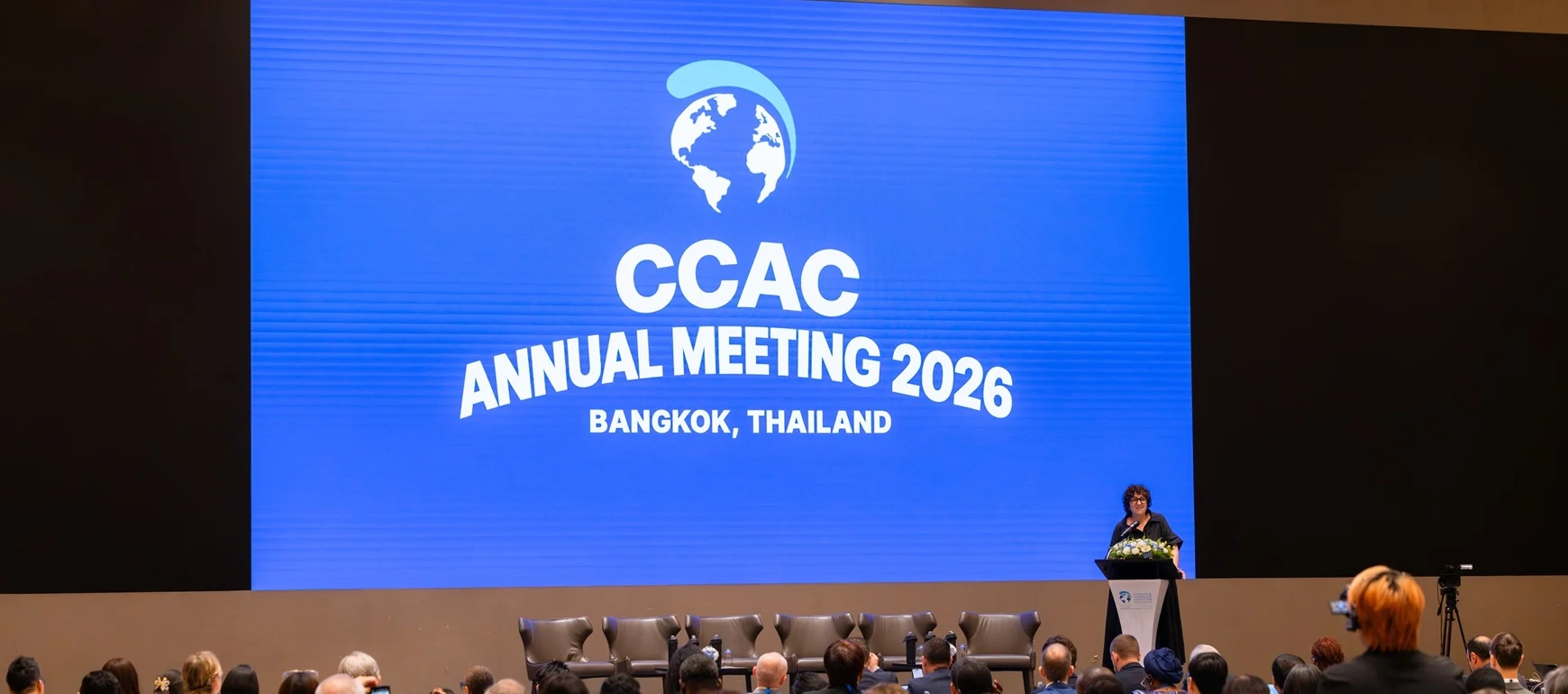 Martina Otto of the CCAC, standing on the stage in a black dress and blue backdrop decalring the conference open.