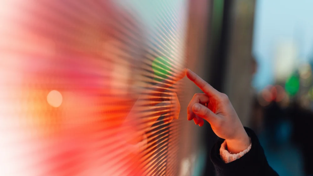A hand poised to touch a LED screen in London.