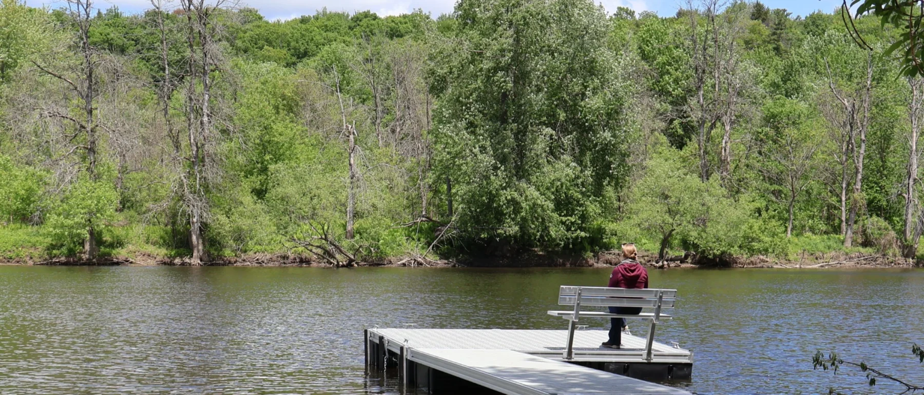Woman sitting on the bridge, looking at the river. Forest on the other side of the river.