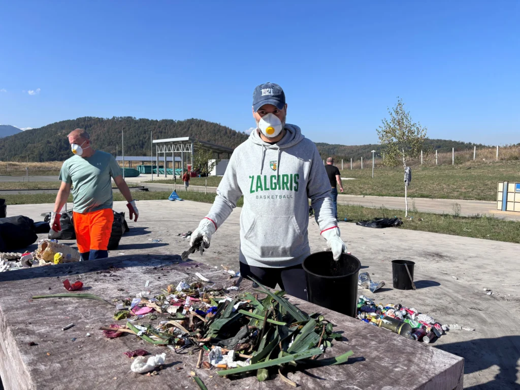 A man in a respirator mask and gloves sorts waste at an outdoor table.