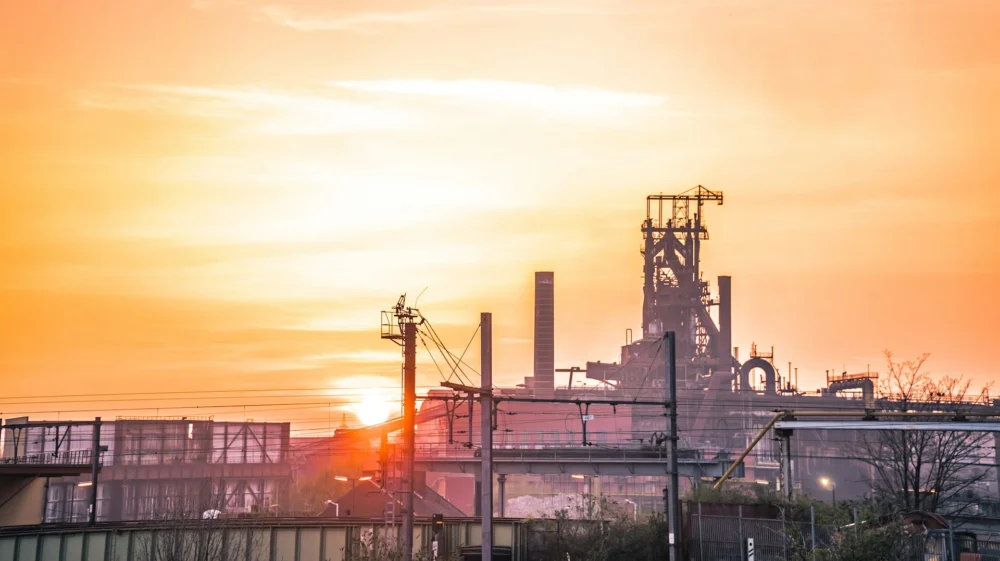 Steelworks blast furnace silhouetted against an orange sunset sky.